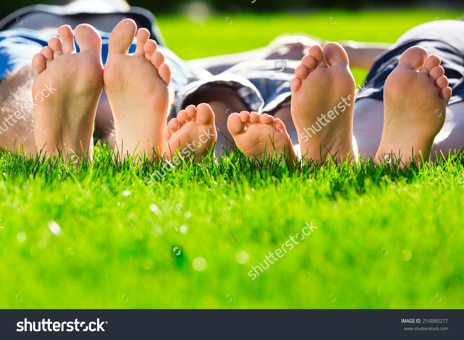 Three people relaxing with bare feet on a grassy lawn